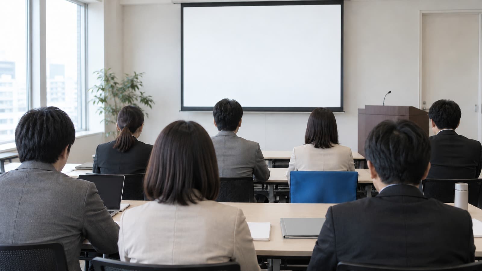 セミナー会場の後方から、机に向かう参加者の背中と前方の白いスクリーンを捉えたドキュメンタリー写真